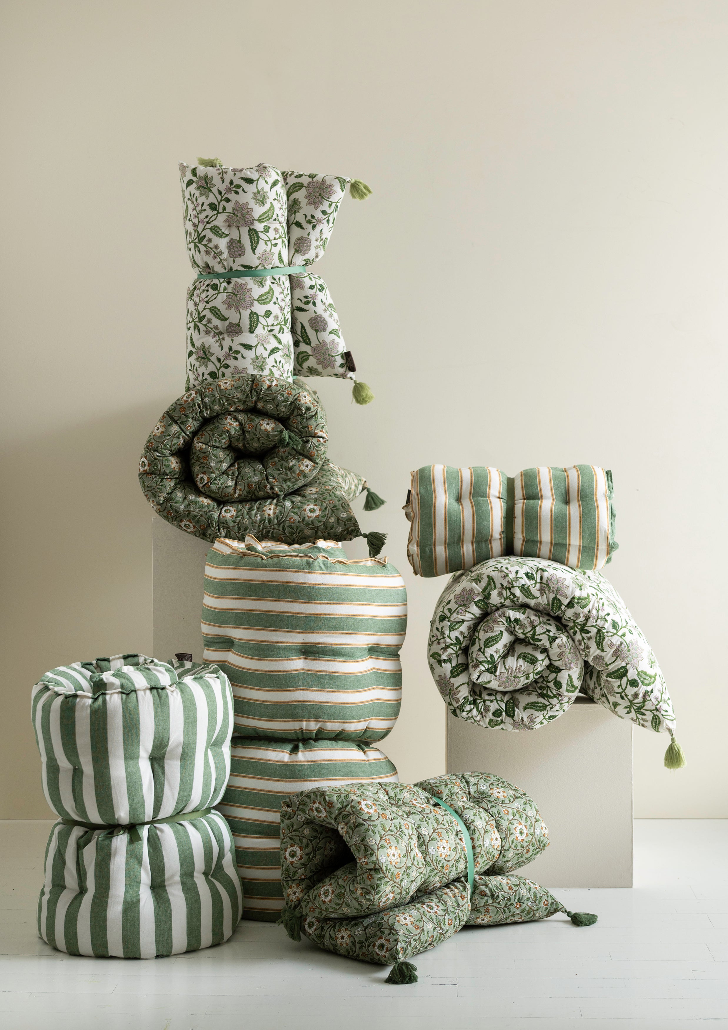 Collection of green and white patterned cushions and pillows on a light background