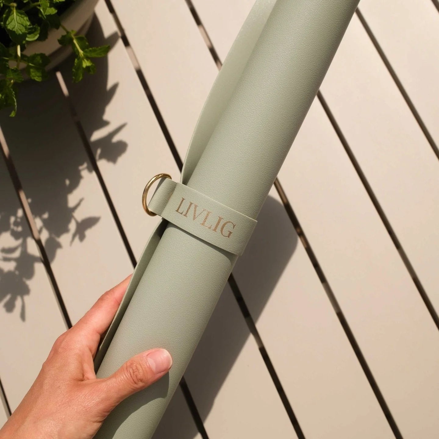 Light green mat with 'LIVLIG' branding held by a hand on a wooden surface.