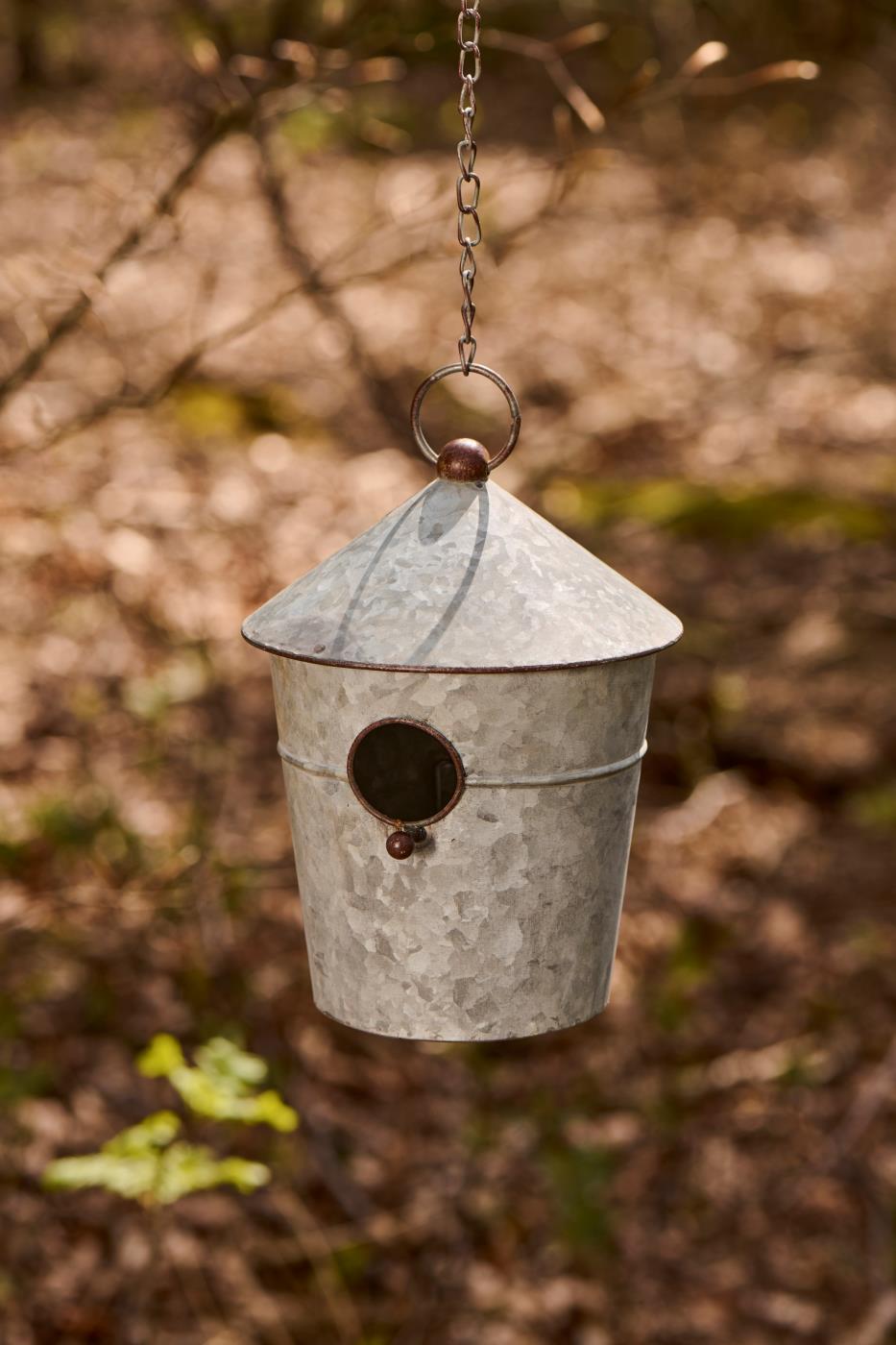 Metal bird feeder hanging from a chain against a natural background