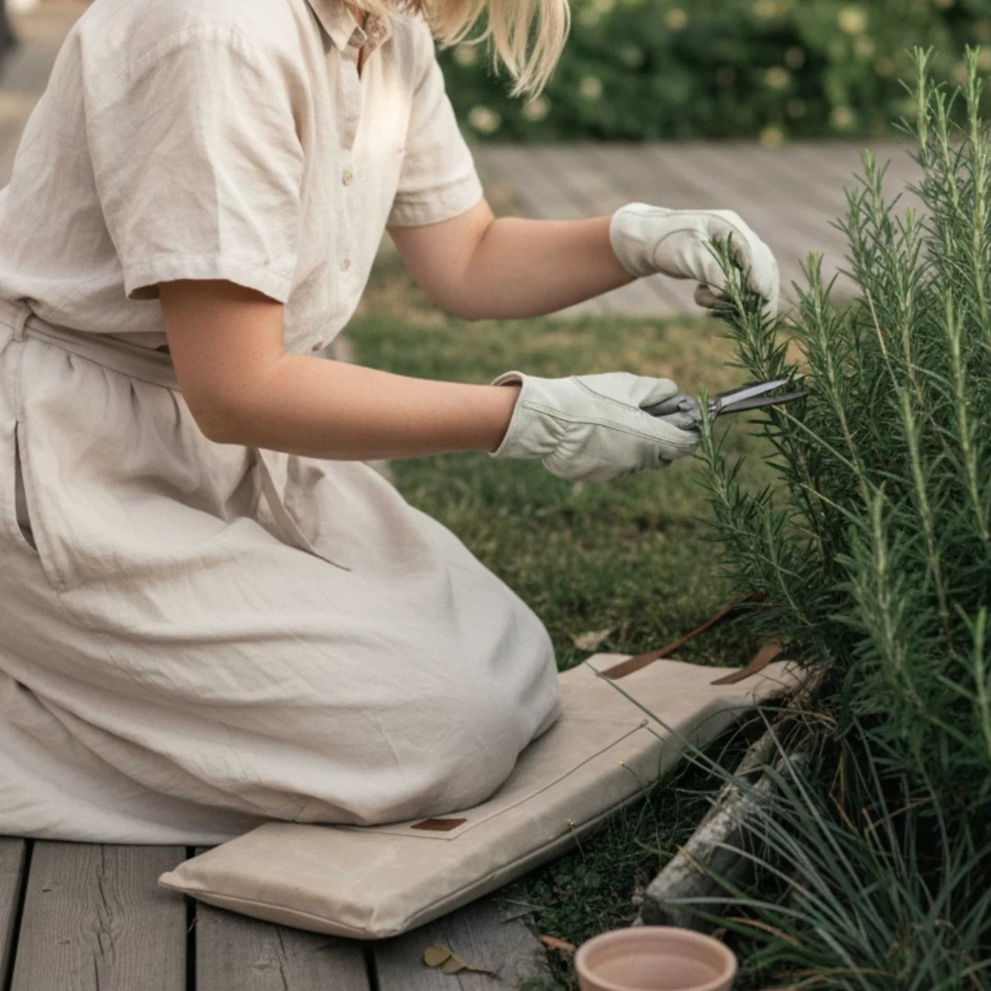 Person in a white apron and gloves pruning a plant outdoors, kneeling on waxed canvas cushion