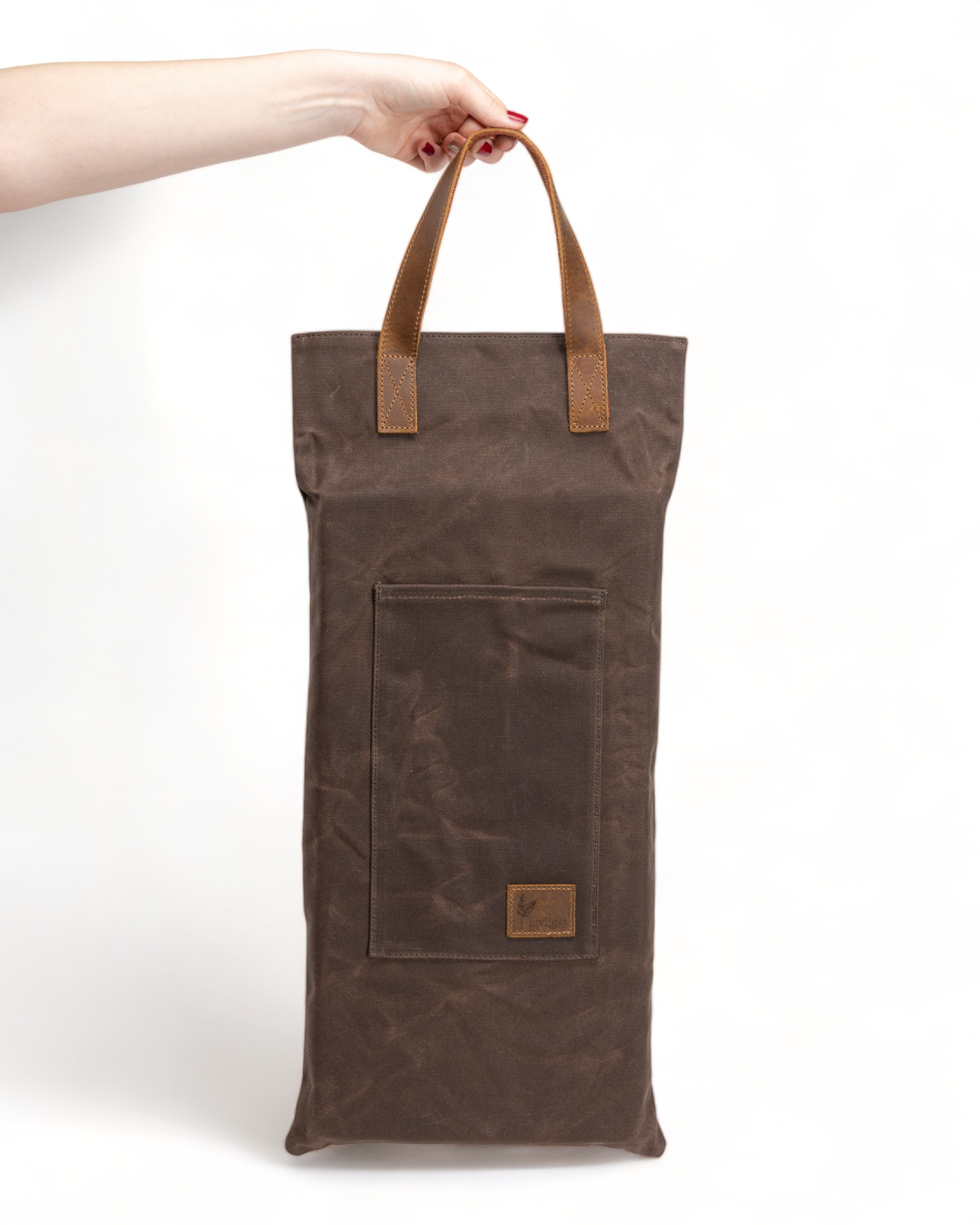 Brown waxed cushion with leather handles held by a hand on a white background