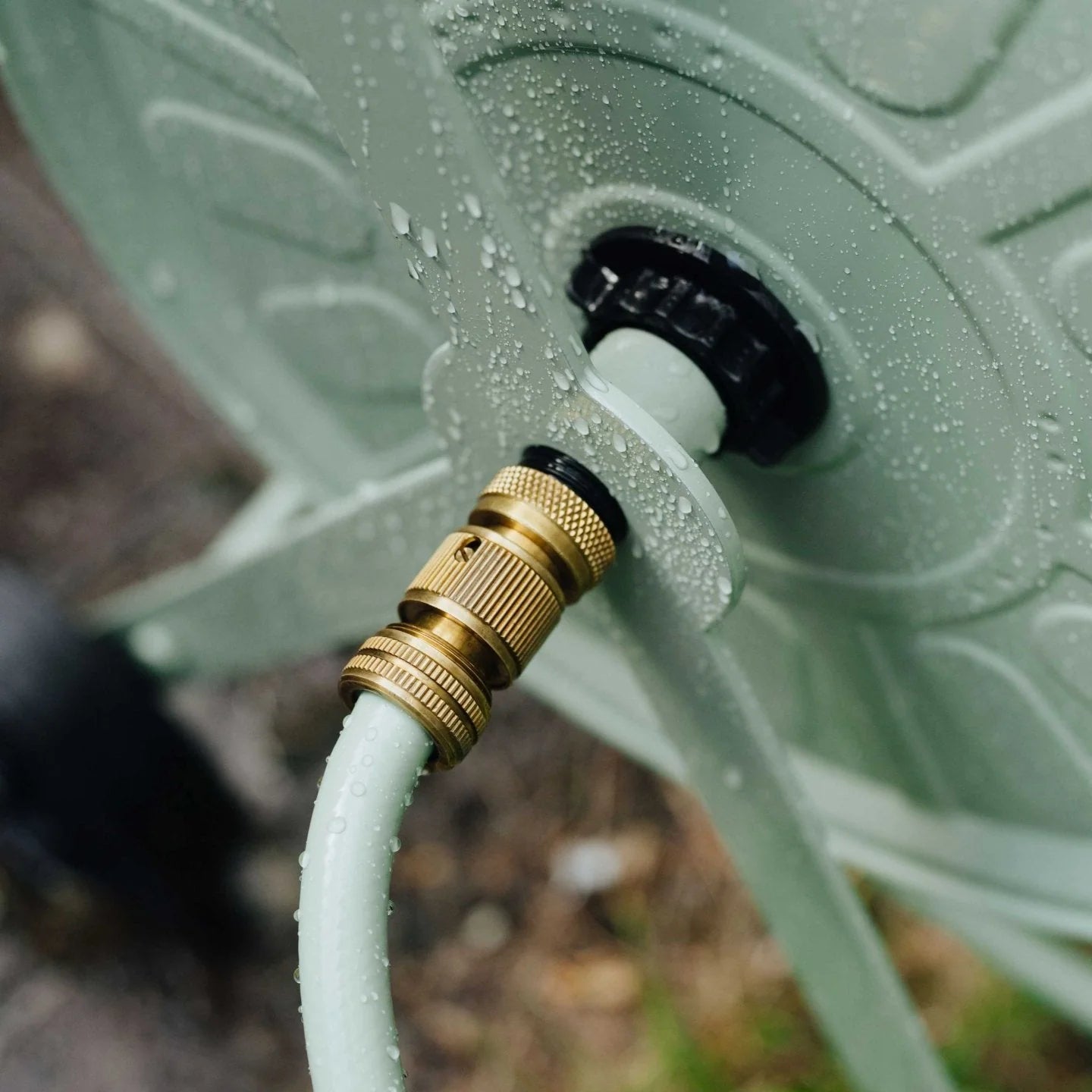 Close-up of a garden hose connection to a green watering can.