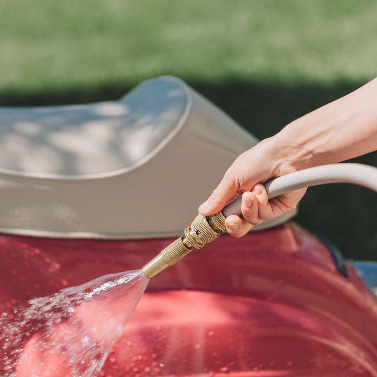 Person washing a red car with a hose, with a blurred green background