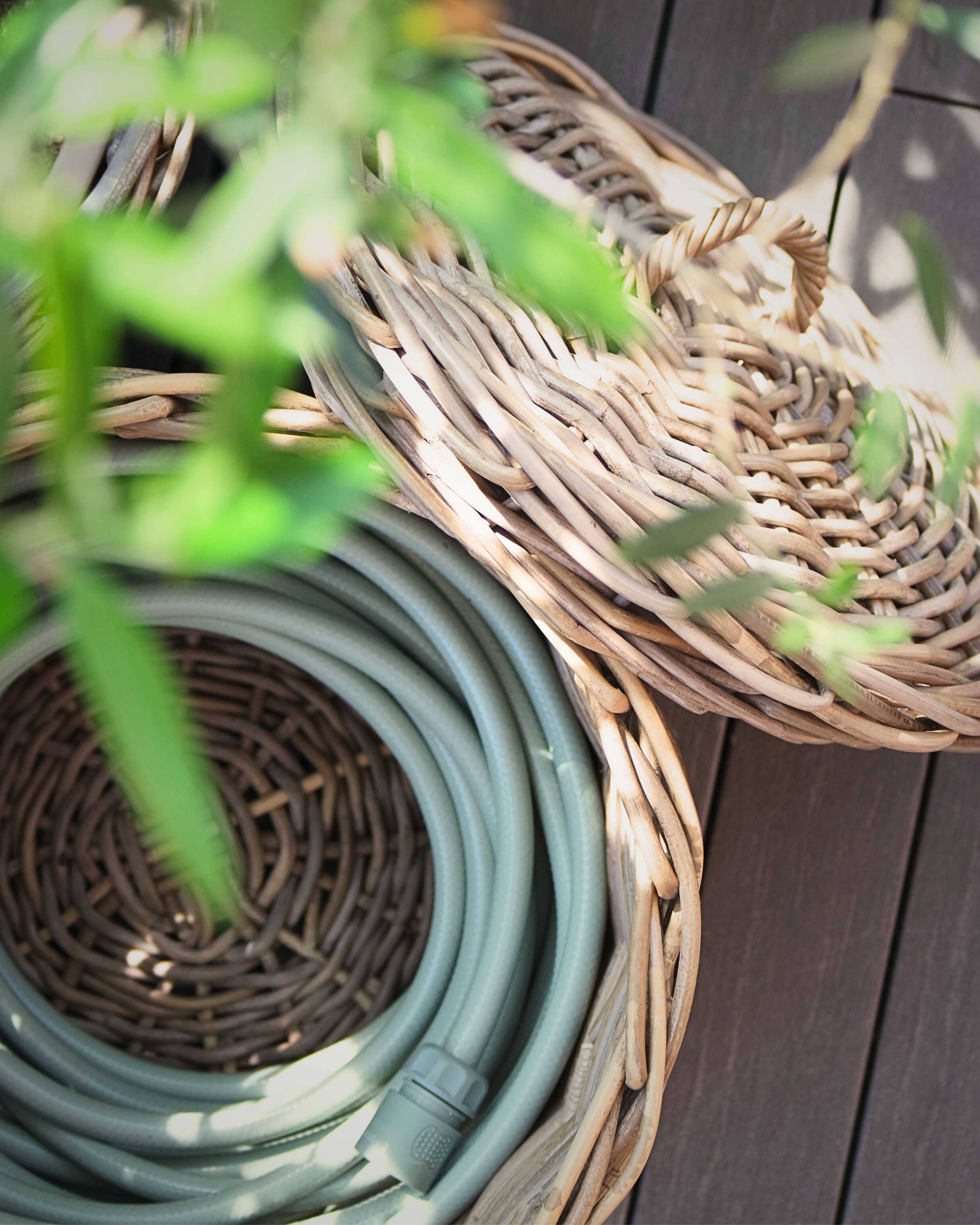 Coiled garden hose on a woven basket with green leaves in the foreground