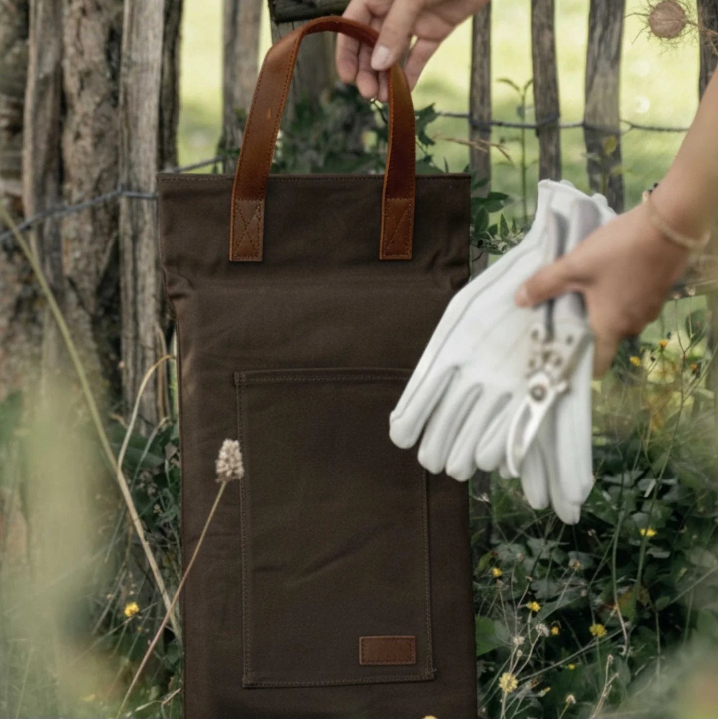 Brown cushion with leather handles held by a hand, surrounded by greenery.