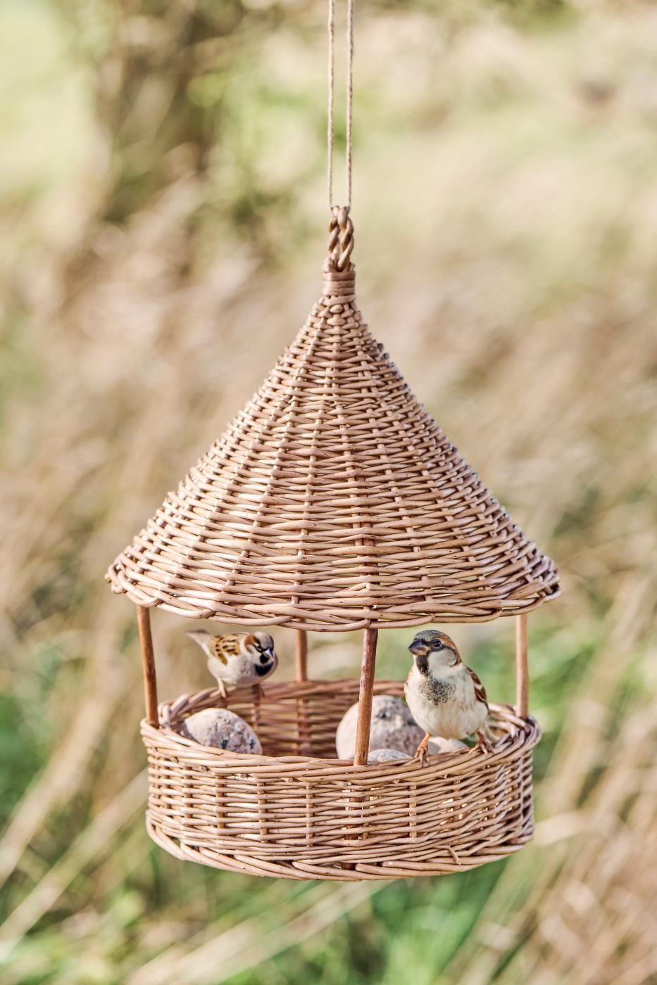 Wicker bird feeder with birds perched on a blurred natural background