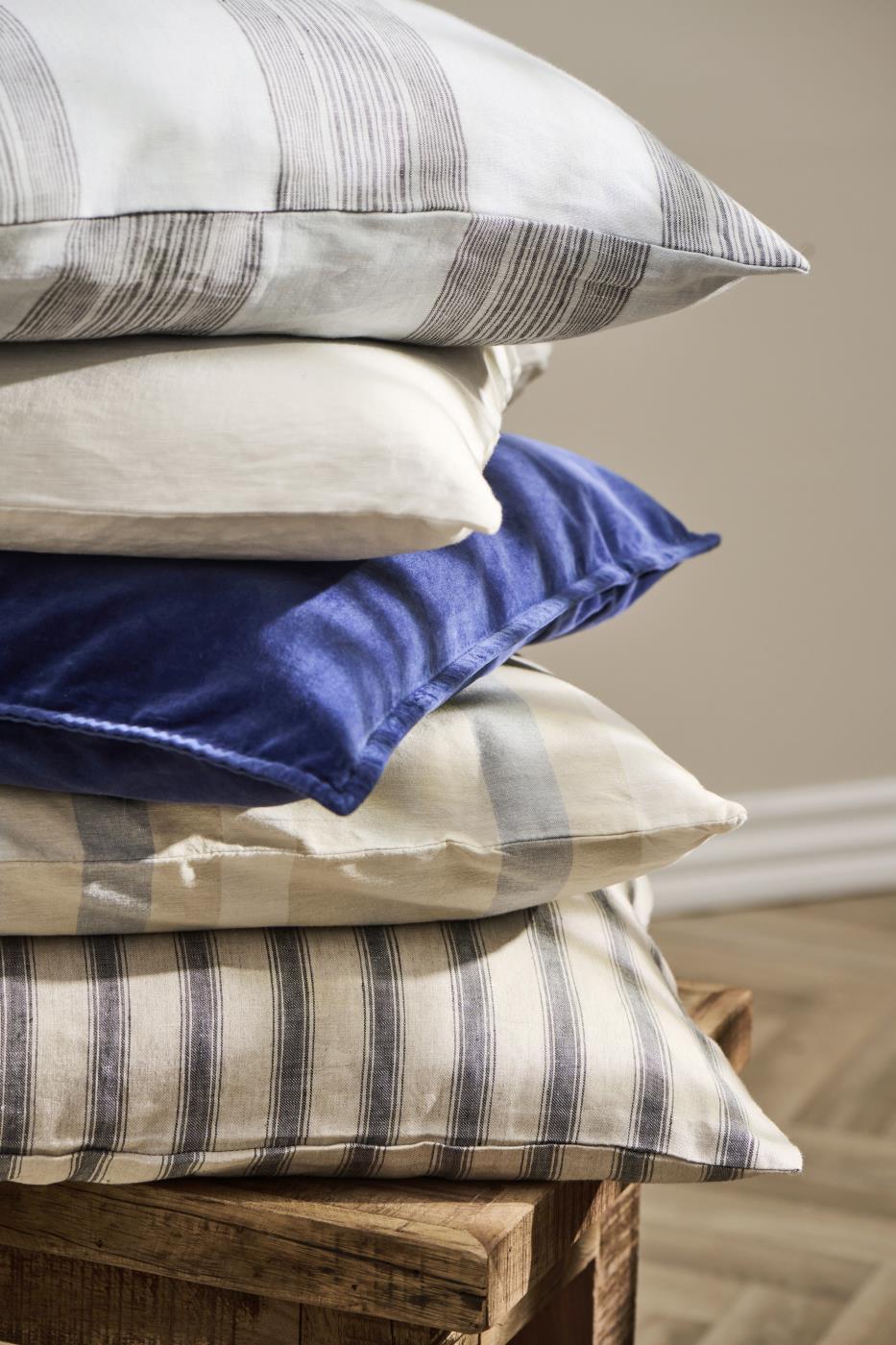 Stack of striped cotton cushions in cream, grey, and charcoal on a rustic wooden crate